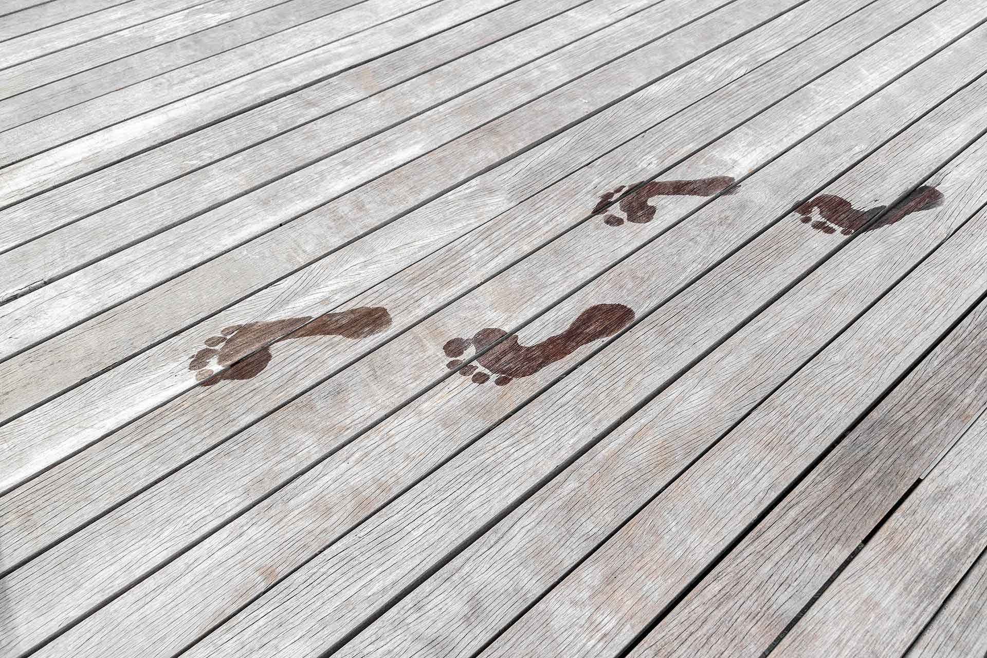 Vergraute Terrassendielen aus Holz mit nassen Fußabdrücken